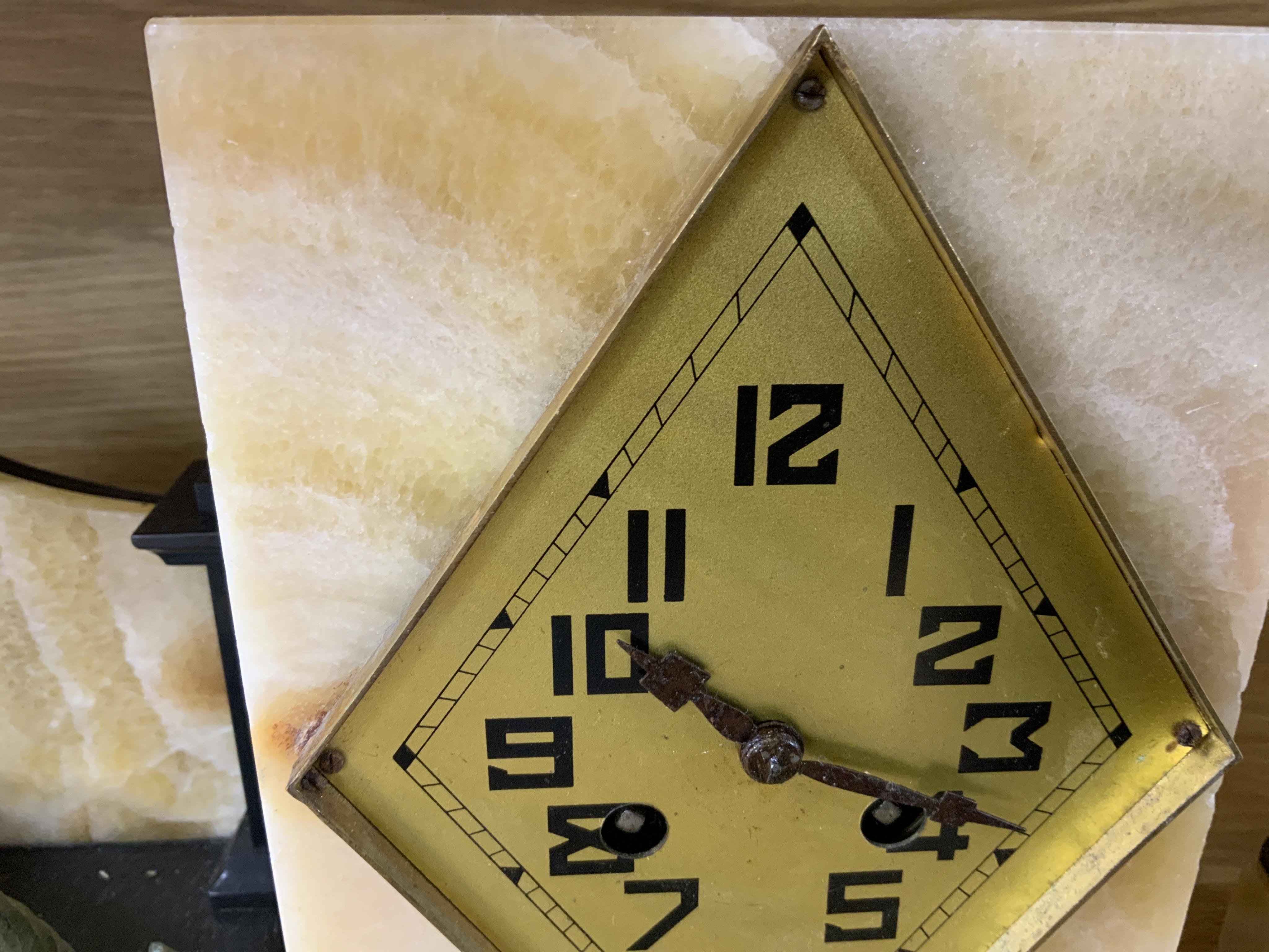 An Art Deco beige onyx and slate clock garniture surmounted with a seated girl holding a bird, 52cm wide